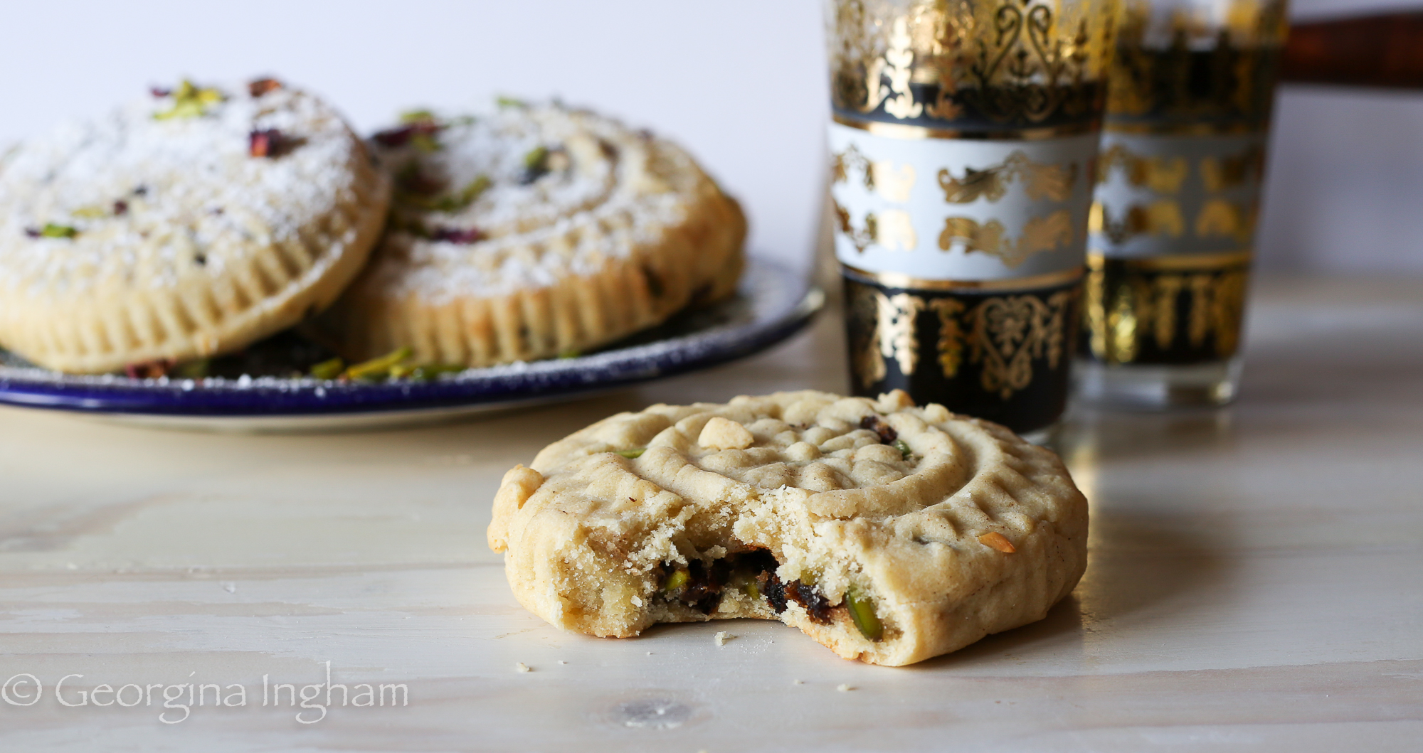 Plate of Ma'amoul cookies served alongside glass cups of Arabic coffee on a table, highlighting the golden pastries and warm coffee tones